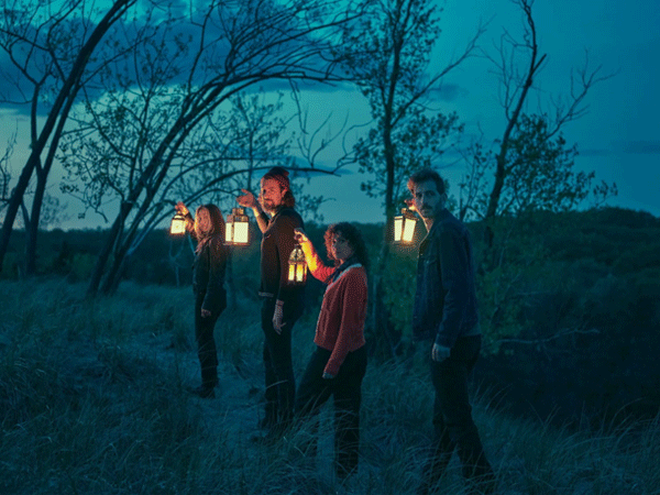 The members of The Crane Wives walking through a forest holding lanterns